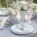 Silver pre-rolled plastic cutlery set arranged on an elegant wedding reception tablescape with white plates and crystal glassware