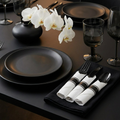 Black pre-rolled plastic cutlery set fanned out on a styled minimalist dinner party table with matte black plates and white orchids
