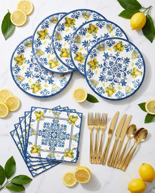 Flat-lay of lemon birthday party tableware set pieces — lemon-print plates, napkins and gold cutlery on marble surface
